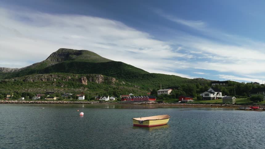 A small yellow rowboat floats serenely in a calm Nordic bay, with a quaint village nestled at the foot of a large green mountain