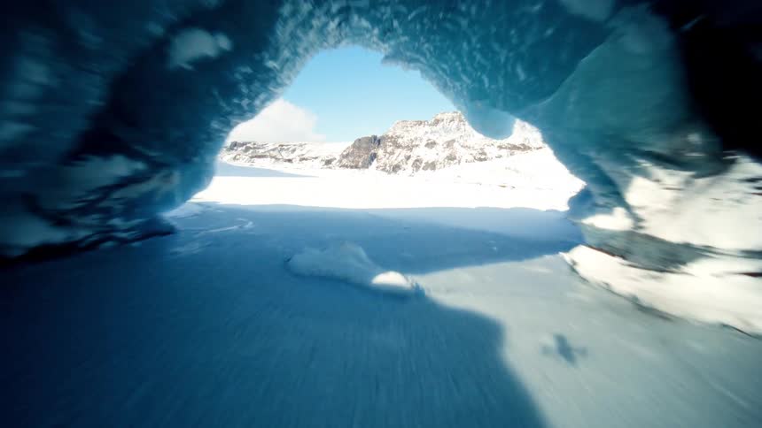 A thrilling FPV drone perspective flying through a breathtaking ice cave in a vast, snowy mountain landscape