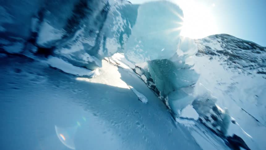 An exhilarating FPV drone flight soars over a snow-covered mountain, diving through a majestic blue ice cave on a glacier