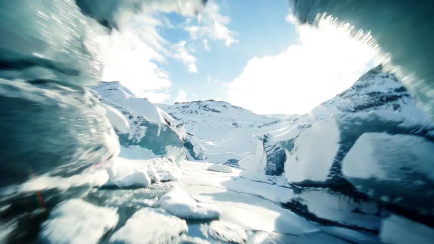 An exhilarating aerial perspective soars through a breathtaking glacial ice cave nestled in a vast, sunlit, snow-covered mountain range