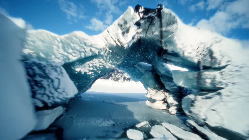 An immersive aerial flight glides through a magnificent ice arch in a snow-covered glacial valley