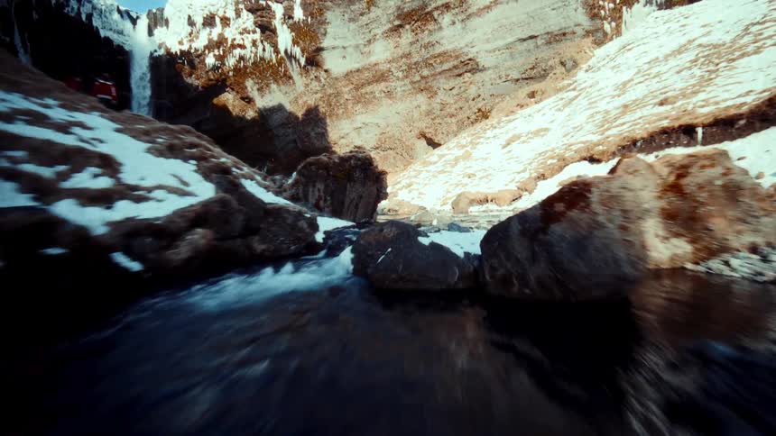 An immersive flight up a rushing river through a snow-covered canyon reveals a stunning waterfall
