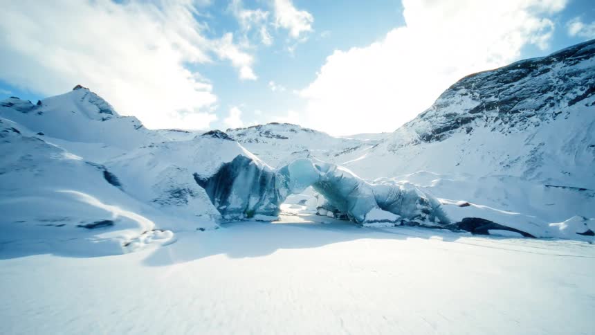 An exhilarating FPV drone flight sweeps over a snowy glacial valley and through a stunning natural ice arch