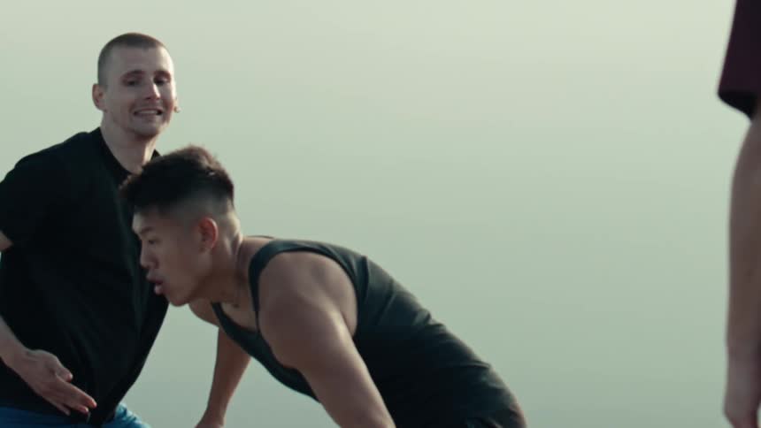 A group of diverse young men play an intense game of street basketball in dramatic slow motion