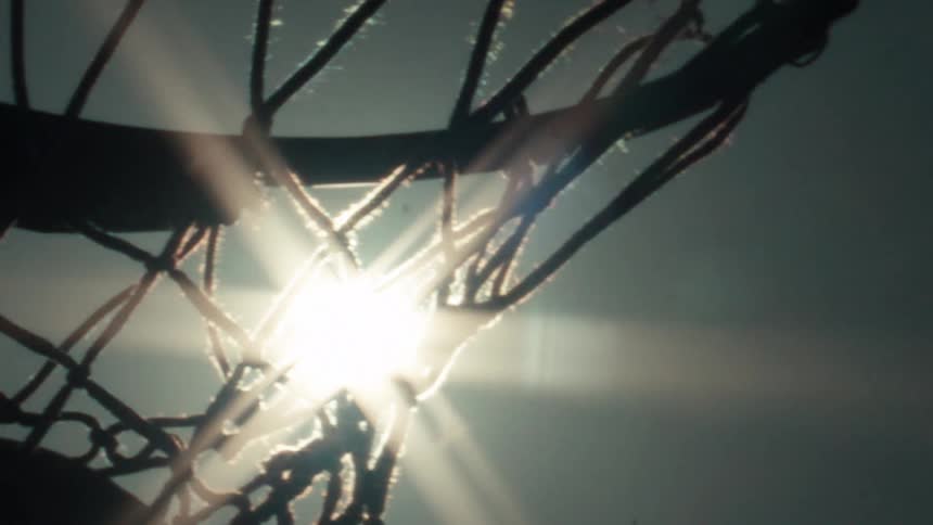 A basketball scores a basket in slow motion, eclipsing the sun as it dramatically passes through the hoop