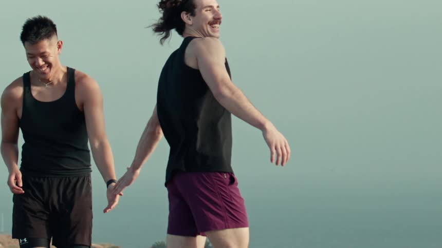 Two athletic friends playfully hold hands in slow motion while enjoying a scenic outdoor view