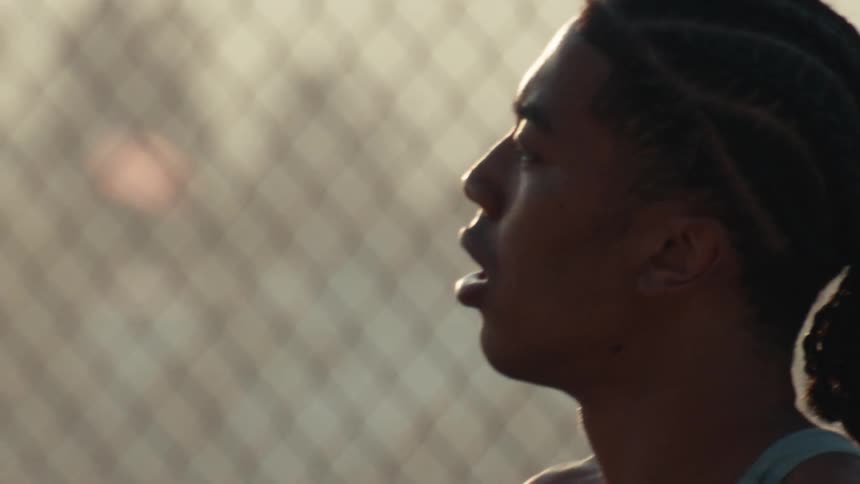Close up slow motion profile of a determined young basketball player catching his breath on a court at sunset