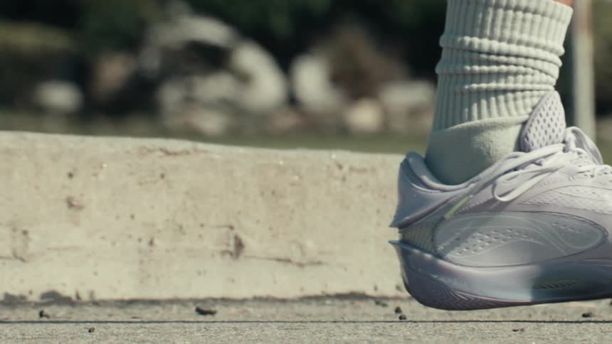 A close-up slow-motion shot captures a basketball bouncing on an outdoor court, followed by a player's shoe landing on the pavement