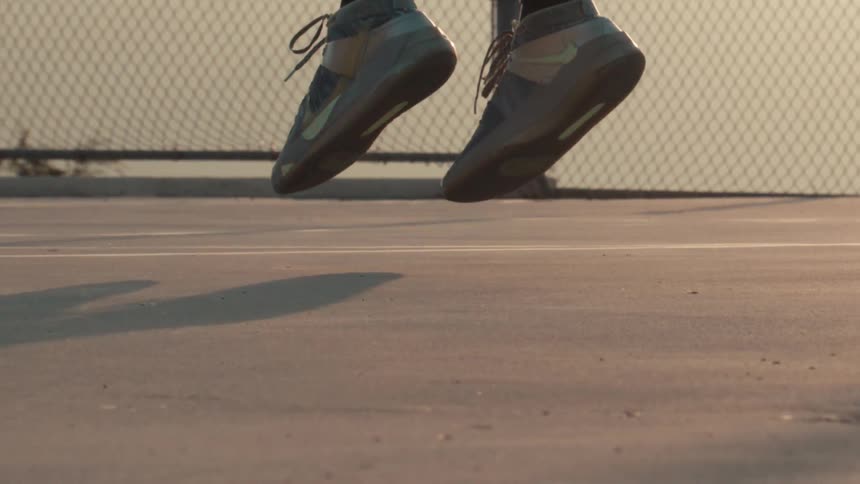A close-up, super slow-motion shot of a basketball player's feet jumping off an outdoor court at sunset