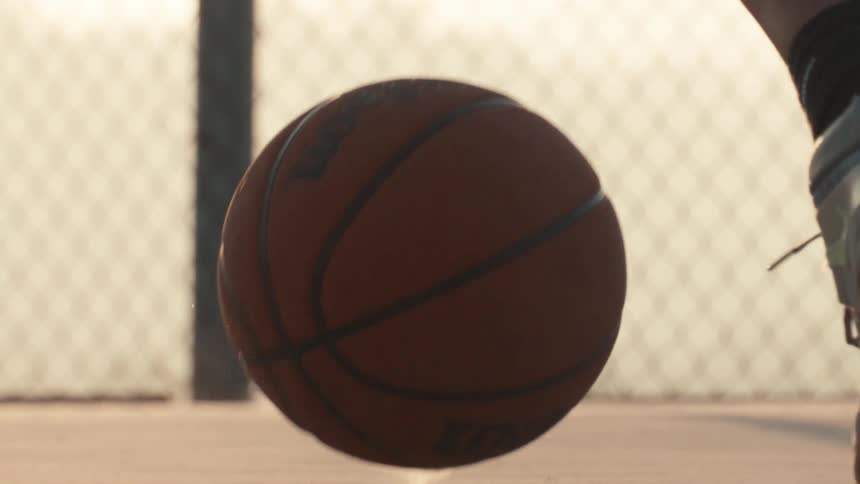 A basketball bounces on an outdoor court in extreme slow motion during a golden sunset