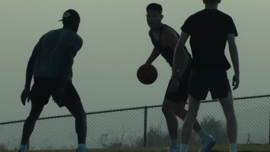 Three friends play a silhouetted game of basketball in dramatic slow motion on an outdoor court