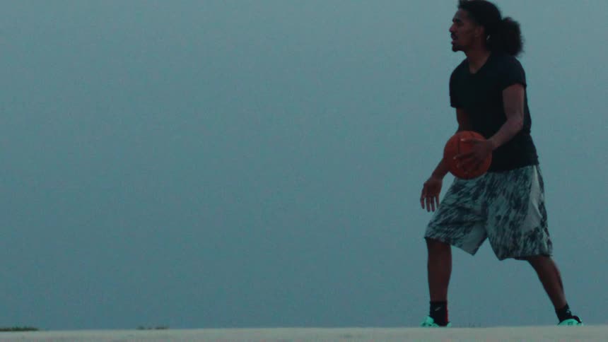 A man dribbles a basketball in dramatic slow motion against a minimalist, moody blue background