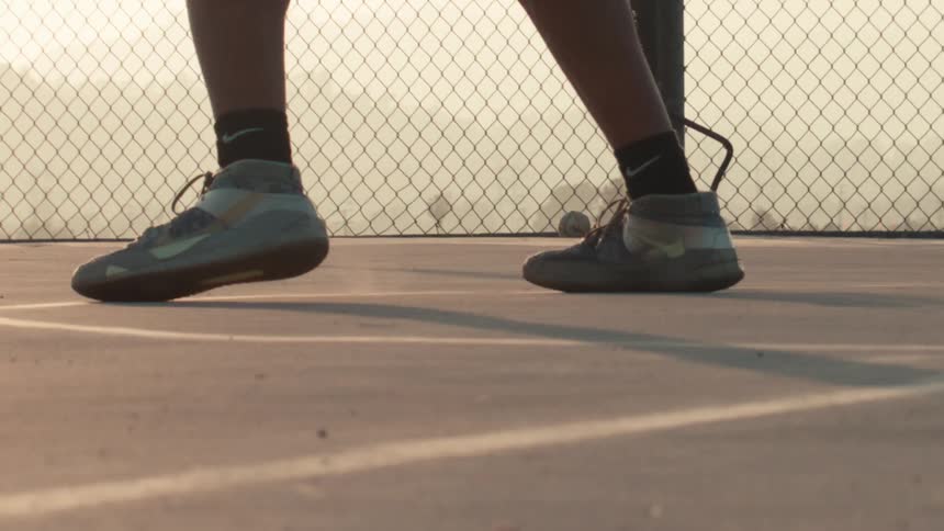 A basketball player's sneakers grip the concrete court in slow motion as they dribble a basketball during golden hour