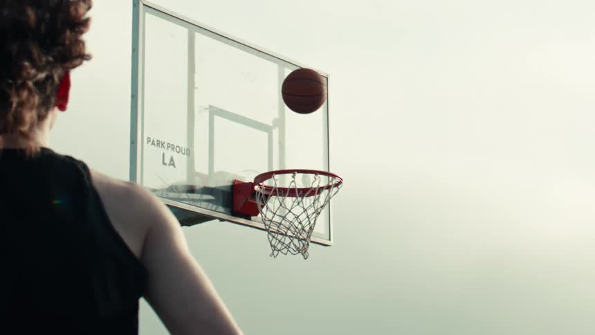 Slow motion over-the-shoulder view of a basketball player missing a shot as the ball bounces on the rim