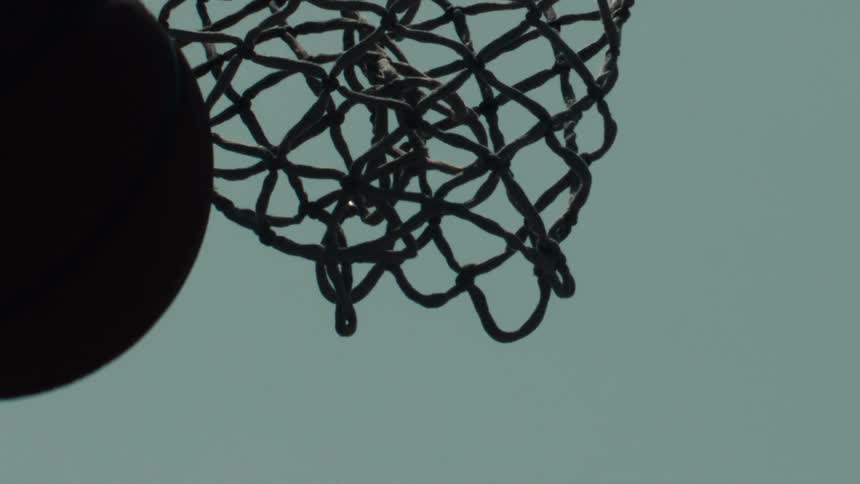 A basketball swishes through a chain net in dramatic slow motion against a clear sky