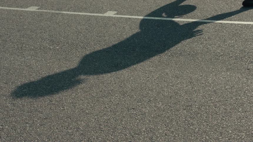 A slow-motion shot of a basketball player's shadow as they dribble a ball on an outdoor court