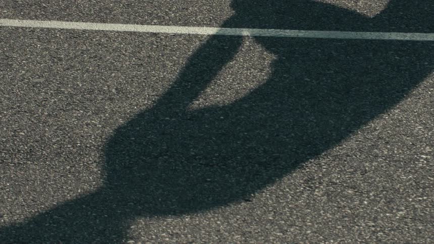 The shadow of a person doing crunches is cast on the asphalt on a sunny day