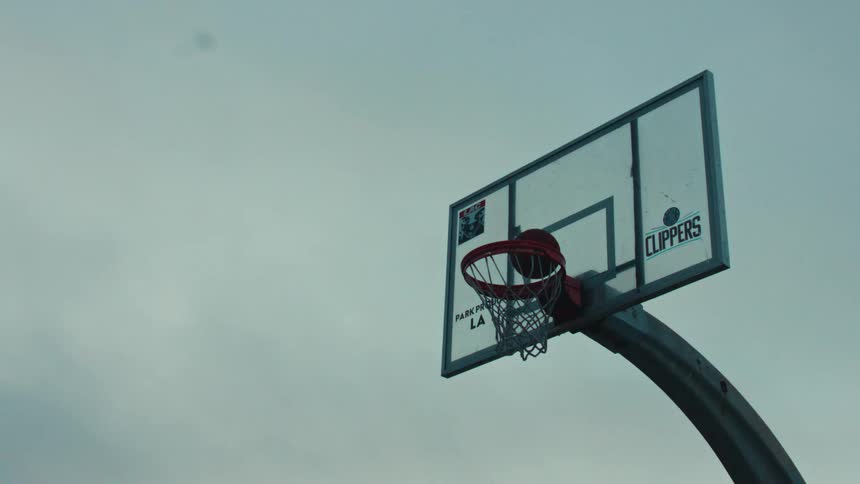 A dramatic slow motion close up of a basketball player dunking a ball into a hoop against a cloudy sky
