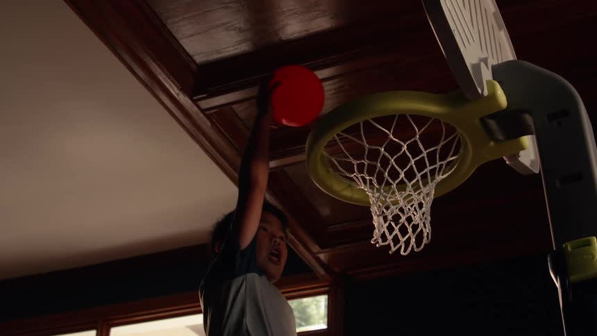 A young boy makes a dramatic slam dunk into a toy basketball hoop in slow motion