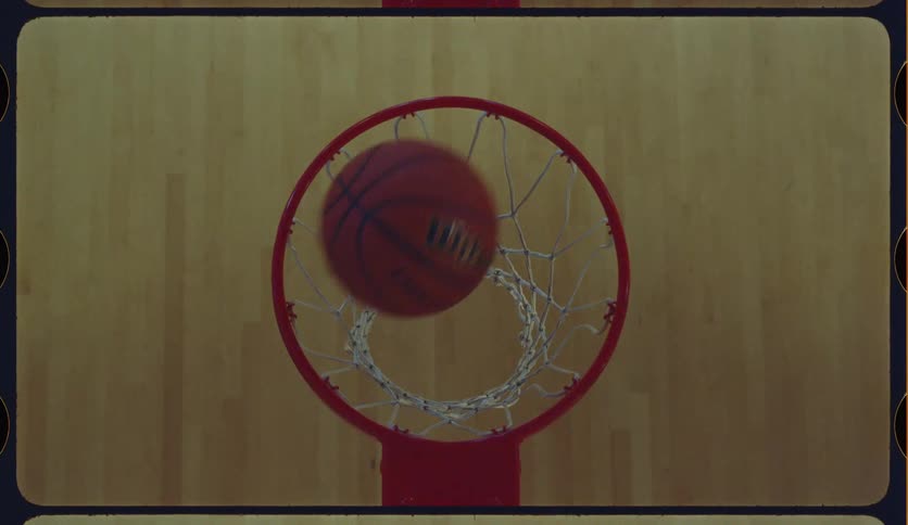 A basketball circles the rim and sinks through the net in a dramatic, slow-motion shot from above