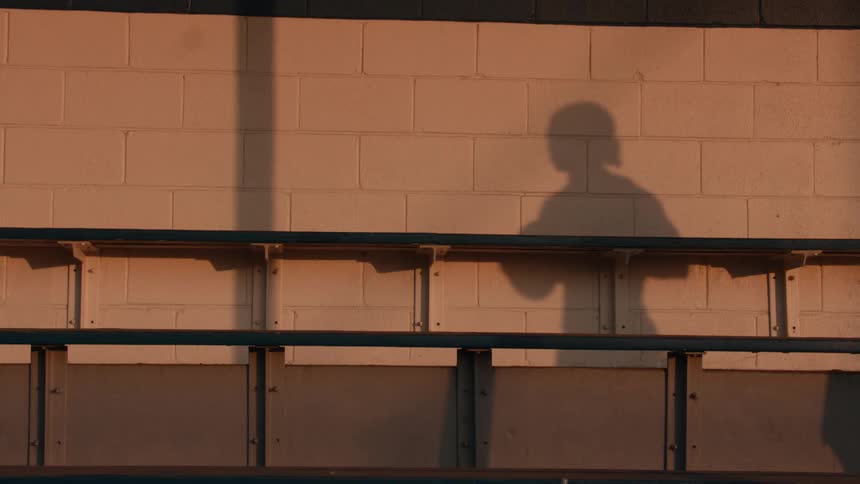 Slow motion shot of a basketball player's shadow dribbling a ball on a brick wall in the warm evening sun