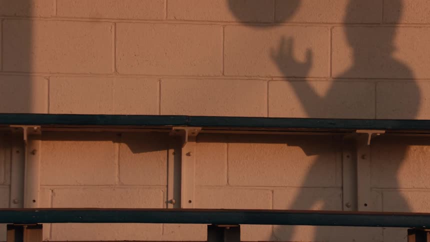 A slow-motion shadow of a person plays with a basketball against a concrete wall during a warm, golden sunset