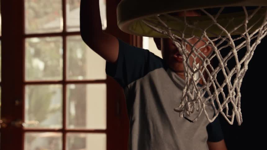 A young boy makes a dramatic slam dunk into a toy basketball hoop in super slow motion