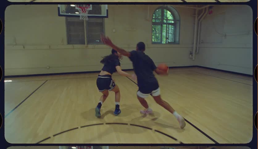 A young man and woman play a competitive game of one-on-one basketball in slow motion on an indoor court