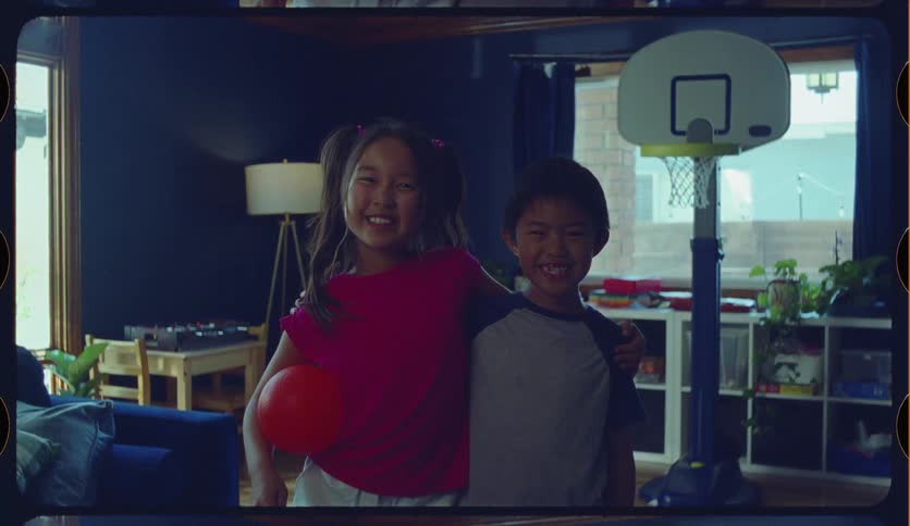 An adorable brother and sister smile for the camera in their playroom in this nostalgic, film-framed clip