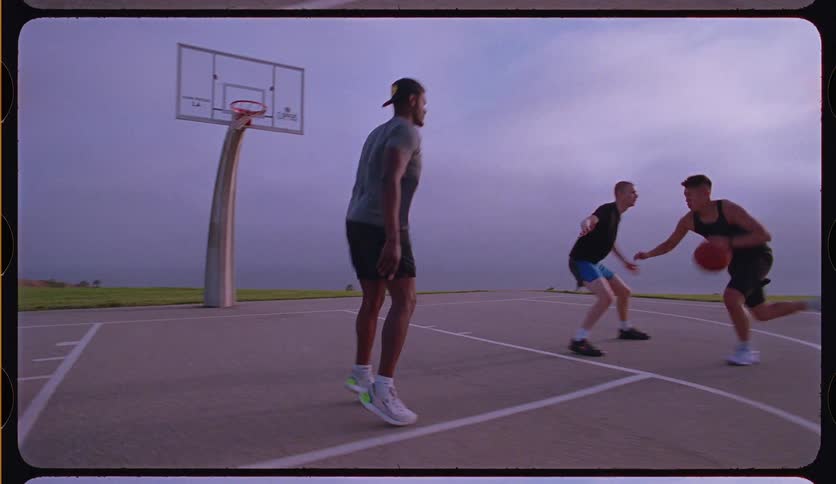 A group of diverse friends plays a game of pickup basketball on an outdoor court, ending with a successful layup in slow motion