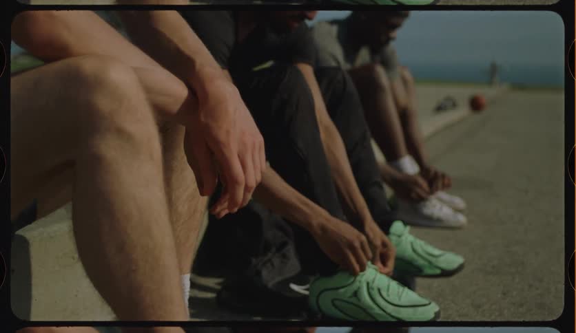 Low-angle shot of a group of basketball players sitting in a row and tying their shoelaces before a game on an outdoor court