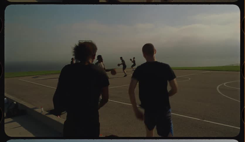 A group of friends greet each other for a game of basketball on a scenic outdoor court by the sea