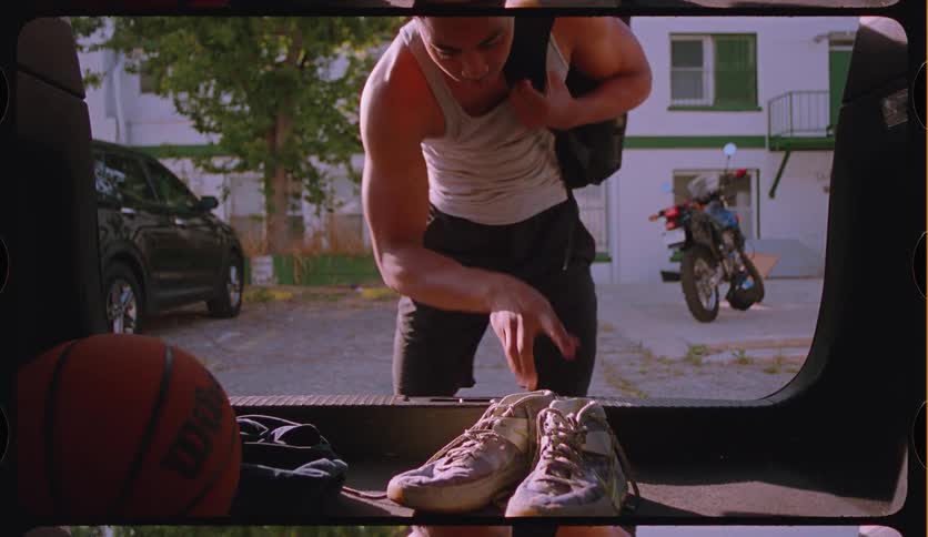 From the perspective of a car trunk, an athletic man grabs his basketball and sneakers before closing the hatch