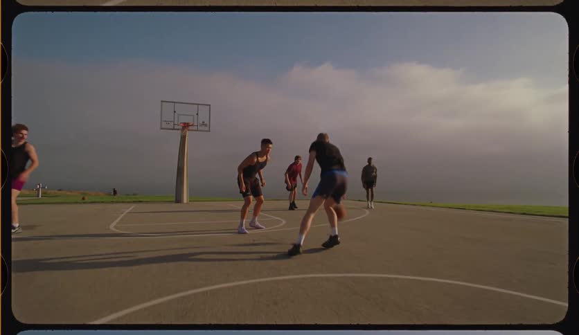 In cinematic slow motion, a group of young men play a pickup basketball game on a scenic outdoor court, ending with a successful jump shot
