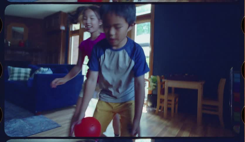 Happy siblings play an energetic game of basketball in their living room in a slow-motion, vintage home movie style