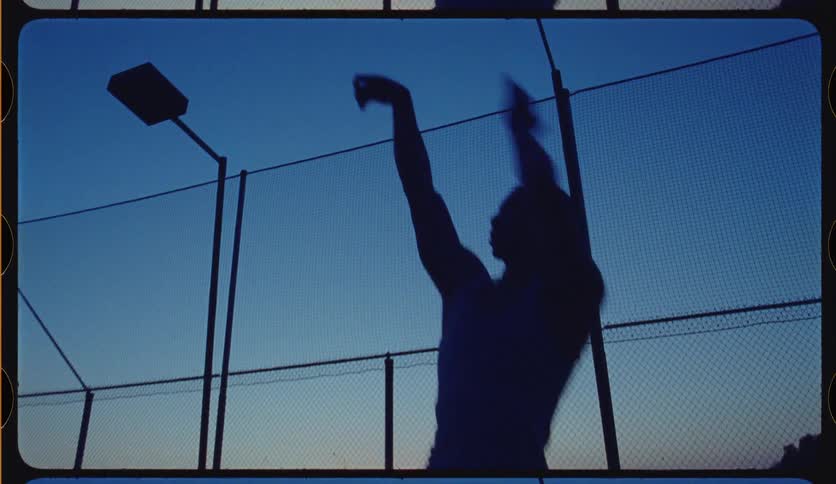 Slow-motion silhouette of a basketball player shooting a basket on an outdoor urban court against the twilight sky