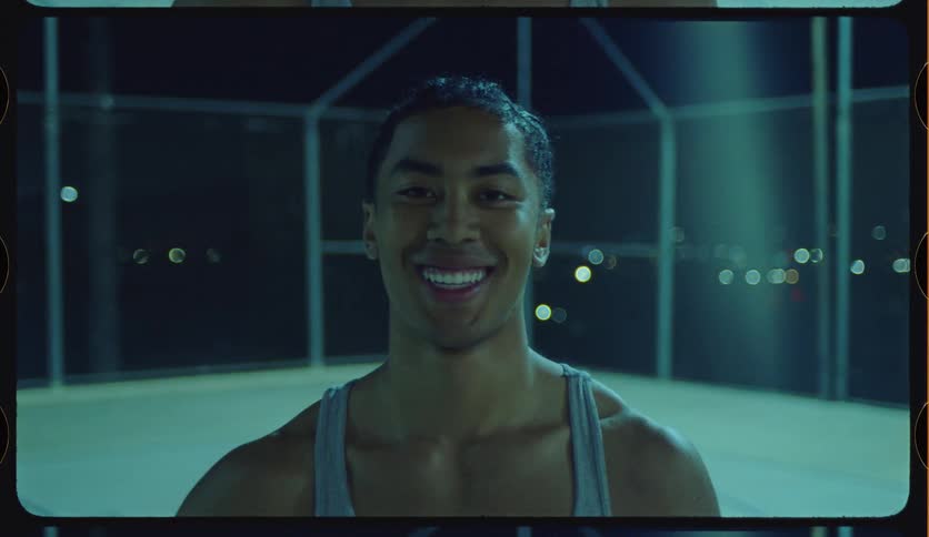 Portrait of a handsome, muscular young man smiling confidently on a sports court after dark, with a cinematic film look