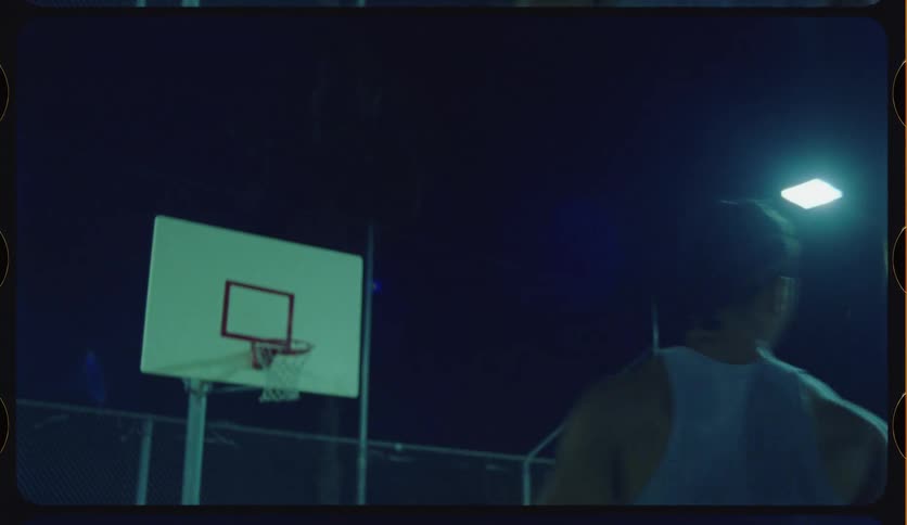 A basketball player makes a perfect swish shot in slow motion on an outdoor court at night