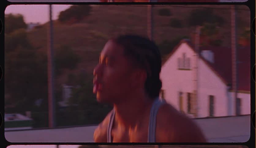An athletic young man with braided hair shoots a basketball in slow motion on an outdoor court, backlit by a beautiful pink sunset