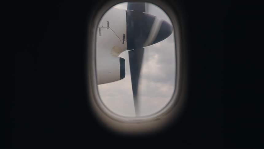 A view from an airplane window shows a propeller spinning rapidly during a flight through the clouds