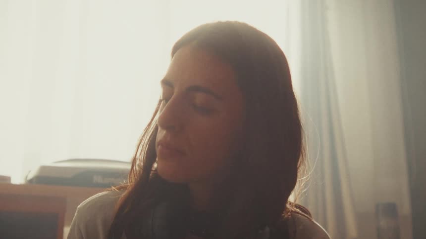 An emotional close-up of a young woman with a pained expression, sitting in a hazy, sunlit room, reflecting on her sadness
