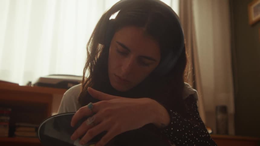 A young woman wearing headphones tenderly holds a vinyl record, lost in a moment of nostalgia in her sunlit room