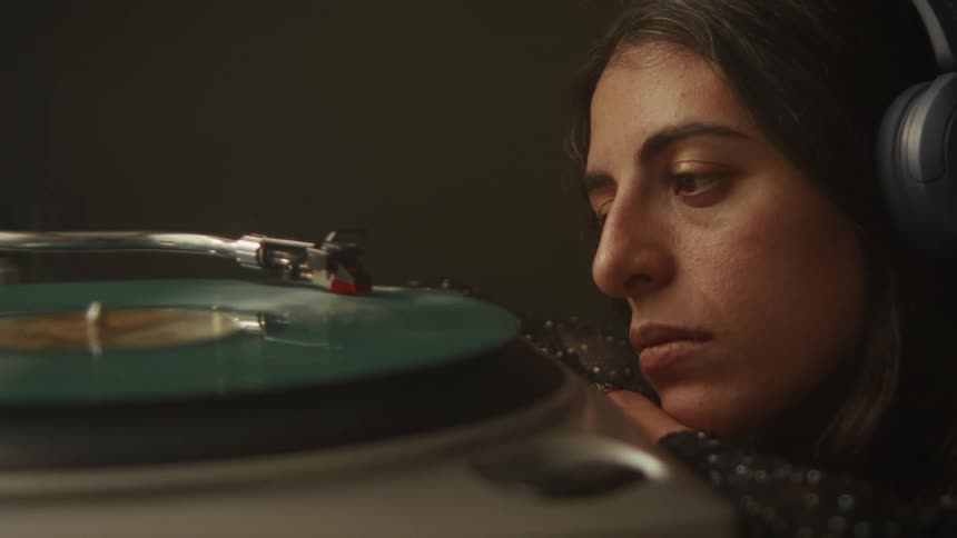 A thoughtful woman wearing headphones rests her head while listening to a spinning vinyl record on a turntable