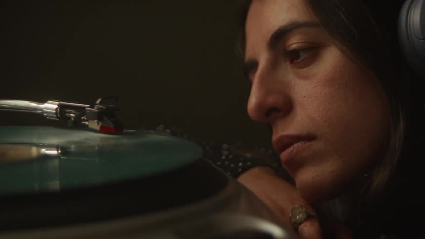 An introspective woman carefully places the needle on a spinning vinyl record and gets lost in the music