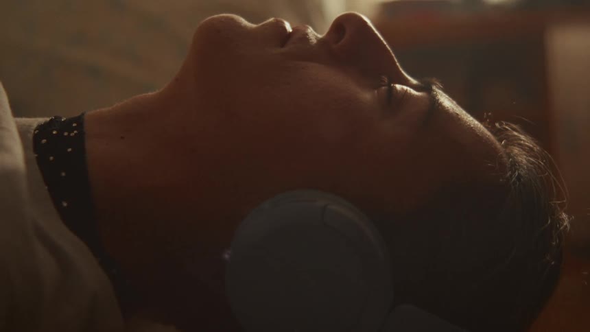 Close-up of a woman peacefully resting with headphones on, eyes closed in a serene, dusty sunbeam