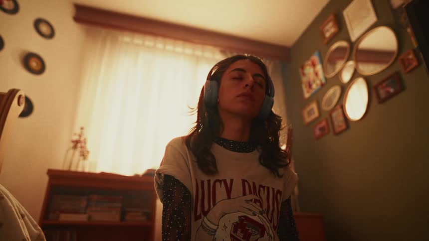 A serene young woman meditates with her eyes closed while listening to music on headphones in her sunlit bedroom