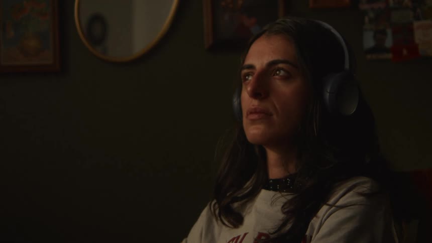 A moody close-up of a focused woman wearing headphones in a dark room, her face illuminated by a screen