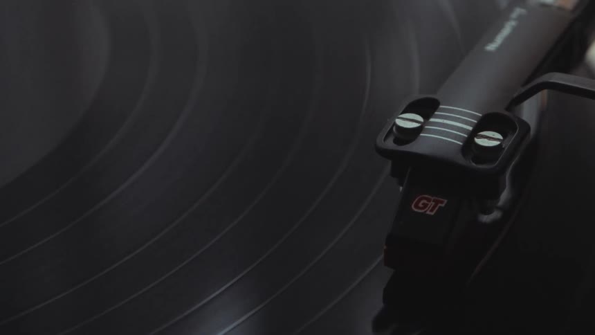 A close-up shot of a record player's needle tracing the grooves of a spinning black vinyl record