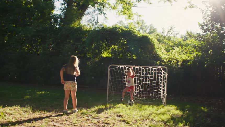 Two young sisters play a friendly game of soccer in their backyard during a sunny afternoon