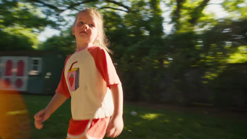 A joyful young girl scores a goal while playing soccer in the backyard and celebrates by running towards the camera